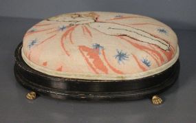 Needlepoint Covered Footstool on Claw Feet Description: Needlepoint Covered Footstool with cupid design, on Claw Feet; 5" h, 17" w.
