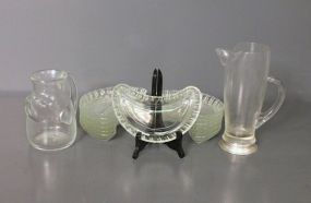  Two Glass Pitchers and Thirteen Clear Glass Bone Dishes Description: Two Glass Pitchers and Thirteen Clear Glass Bone Dishes, dishes (8" l., 4" w.) one pitcher is 6 3/4" h., other pitcher is 9 3/4" h.