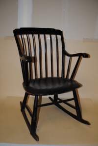 STEP DOWN WINDSOR ARMCHAIR ROCKER; spindle back with plank seat, painted black; holes possibly for a restraining device,