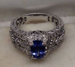 One stamped 18KT white gold lady's cast sapphire and diamond ring with a flat tapered shank with a bright polish with engraving finish. Containing: One prong set oval standard brilliant cut natural blue sapphire, measuring 7.95 x 5.38 x 3.65mm, 