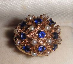 One 10-14KT yellow gold lady's cast sapphire and pearl cluster ring with a filigree shank with a bright polish finish. Containing: Nine prong set round standard brilliant cut synthetic blue sapphires, measuring 3.10-3.00 x 1.98mm, approximate to