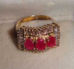 One stamped 14KT yellow gold lady's cast 3 ruby and diamond ring with a tapered shank with a bright polish finish. Containing: Three prong set oval standard brilliant cut synthetic rubies, measuring 5.10 x 4.10 x 2.67mm, 15% bulge factor, approx
