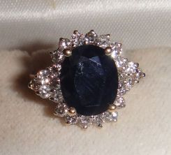 One stamped 14KT yellow gold lady's cast sapphire and diamond cluster ring with a split shank with a bright polish finish. Containing: One prong set oval standard brilliant cut natural blue sapphire, measuring 11.00 x 9.17 x 4.00mm, 6% bulge fac