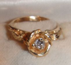 One 10-14KT yellow gold lady's cast diamond rose ring with a leaf pattern shank with a bright polish with relief finish. Containing: One prong set round brilliant cut diamond, measuring 3.75-3.70 x 2.24mm (depth est.) approximate weight of 0.19c